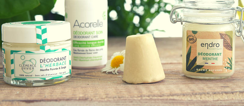 Plusieurs déodorants naturels et bio posés sur une table devant des plantes.